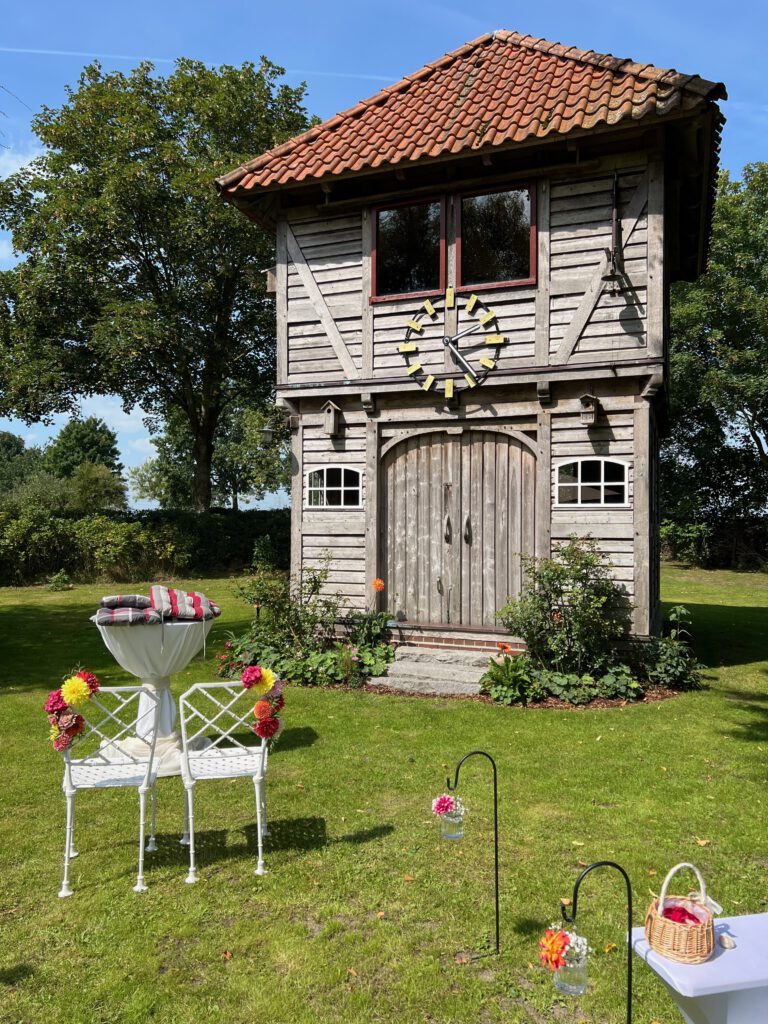 Uhrenturm mit festlich dekoriertem Trautisch und Stühlen bei einer Gartenhochzeit