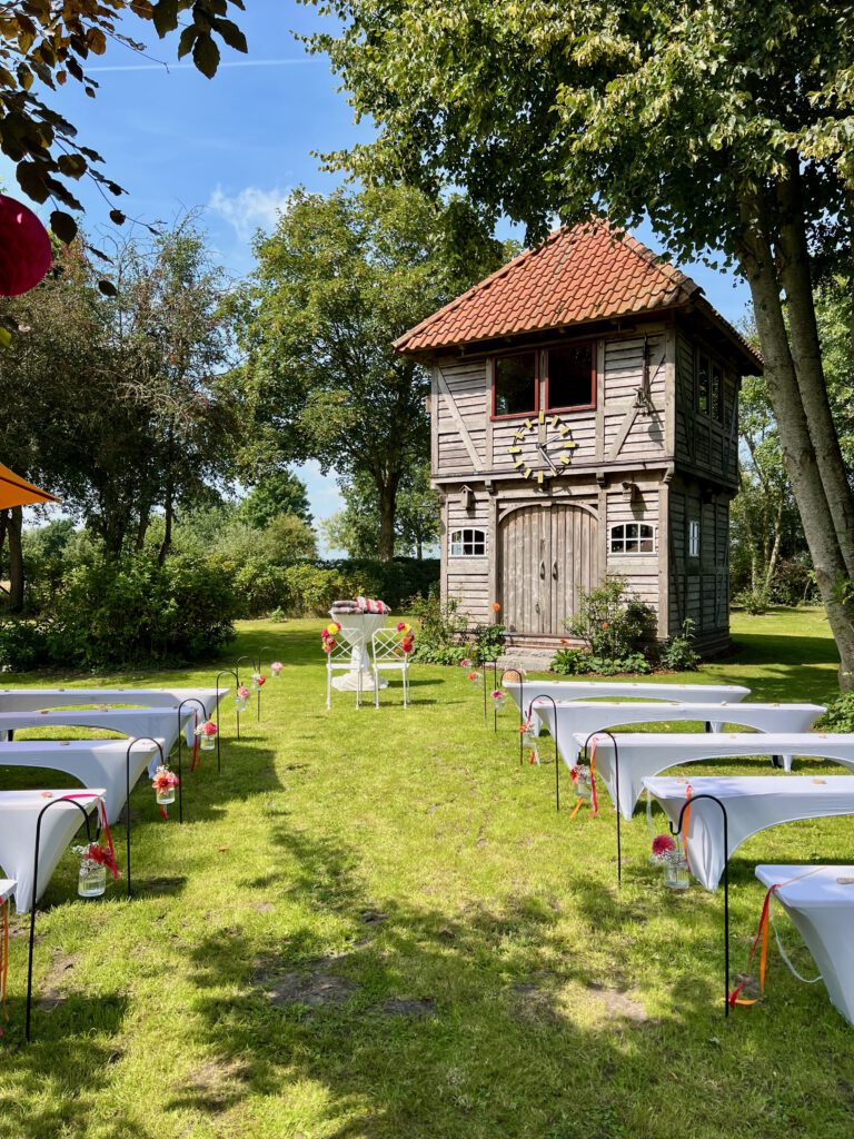 Gartenhochzeit mit Stuhlreihen, Blumendeko und Uhrenturm im Hintergrund