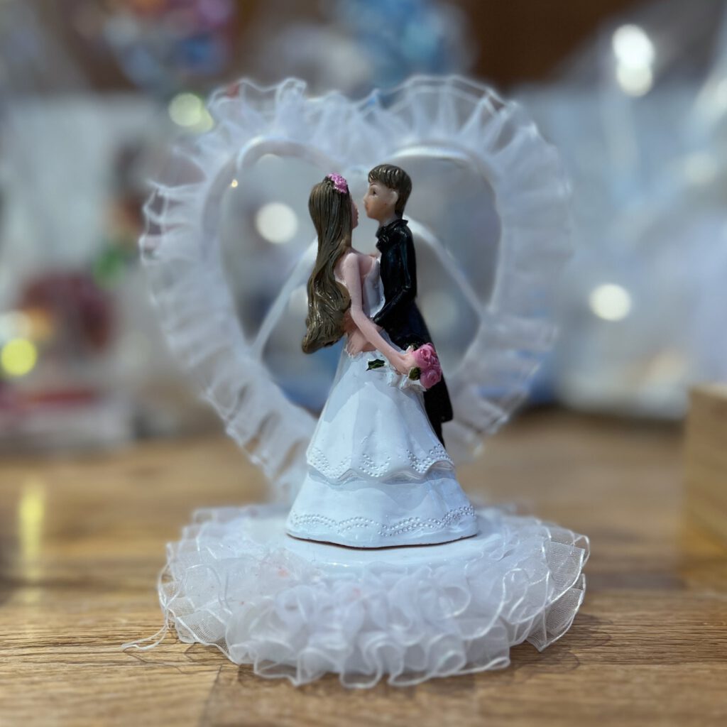 Hochzeitstortenfigur mit Braut und Bräutigam vor einem Herzrahmen auf Holzuntergrund
