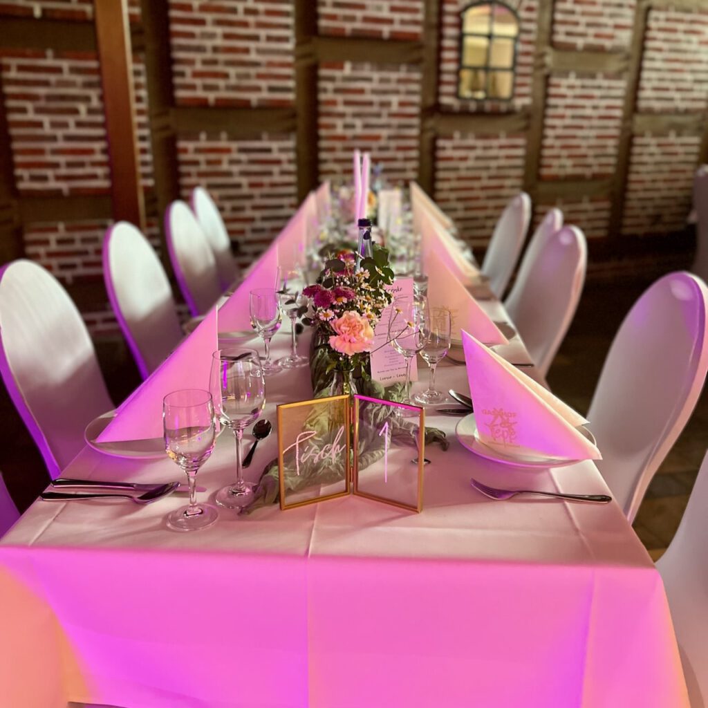 Festlich gedeckte Hochzeitstafel mit Blumendekoration und pinker Beleuchtung im Gasthof Tepe Aschendorf