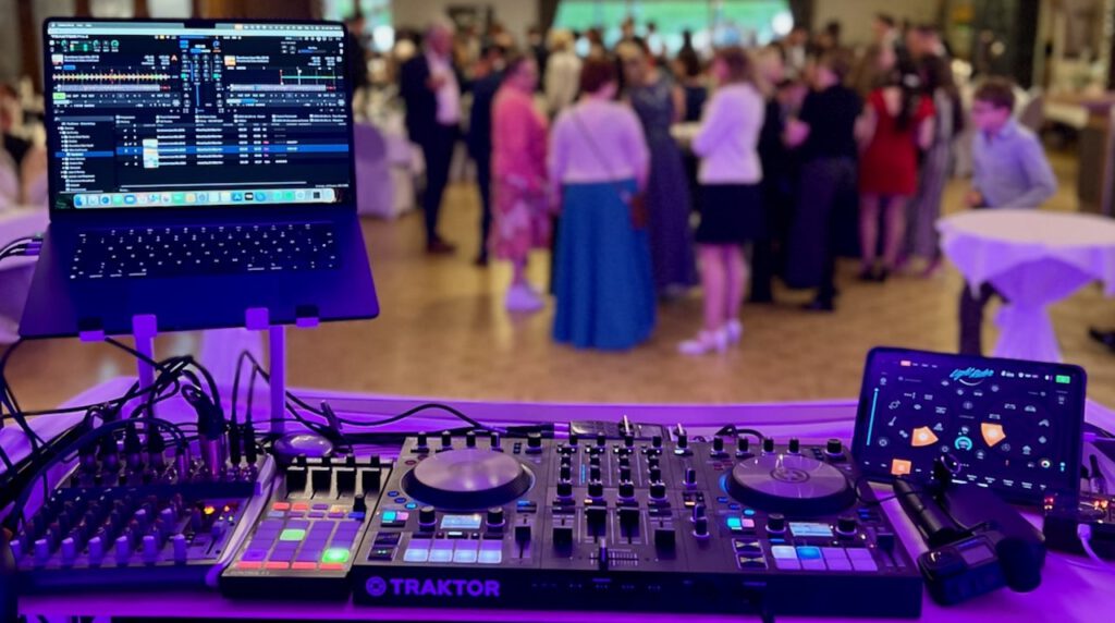 DJ-Pult mit Mischpult, Laptop und tanzenden Gästen im Hintergrund bei der Hochzeit im Gasthof Tepe