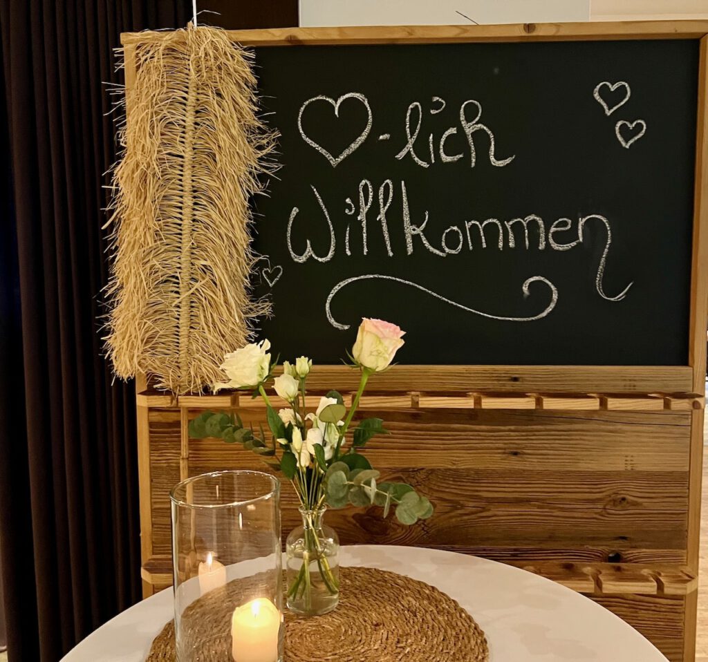 Willkommensschild mit Blumen und Kerze bei der Hochzeit von Tabea und Heiko im Heidekrug Bentstreek