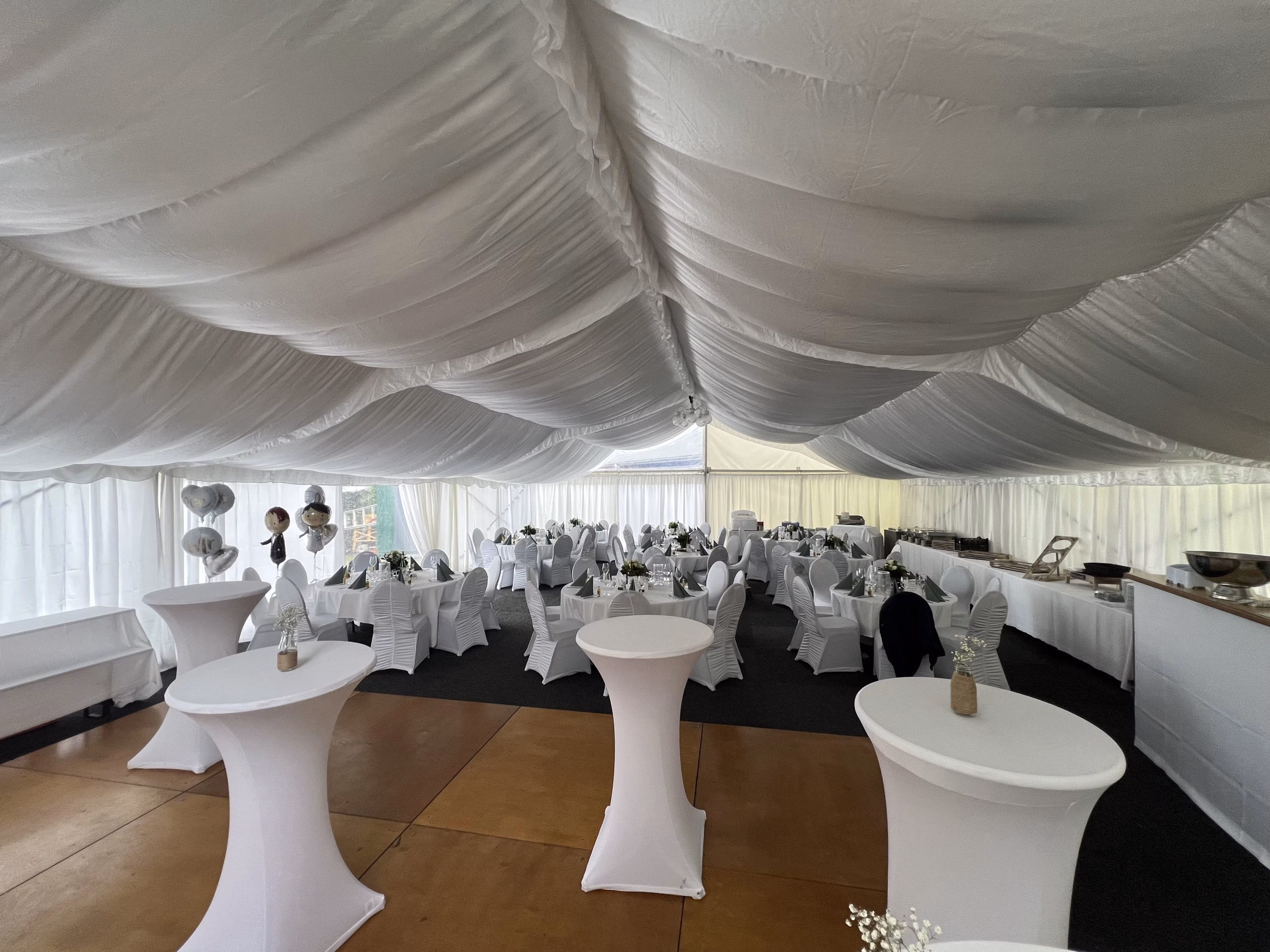 Tanzfläche und runde Hochzeitstische mit weißen Hussen im Zelt am Banter See