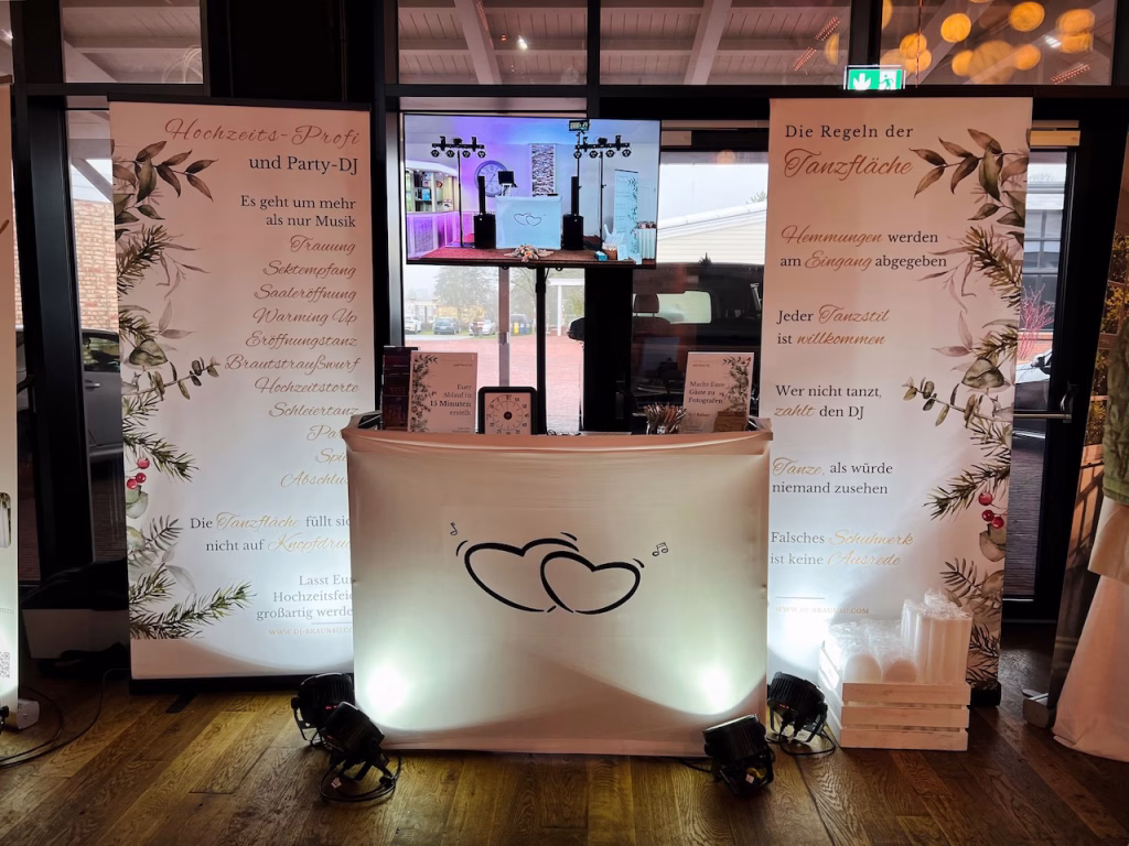 Der beleuchtete Messestand von Hochzeits-DJ Harald Braun auf der Hochzeitsmesse am Meer im Wangerland Resort. Zu sehen ist das weiße DJ-Pult mit Herz-Logo, ein Bildschirm und zwei große Banner mit den Aufschriften "Hochzeits-Profi und Party-DJ" und "Die Regeln der Tanzfläche".