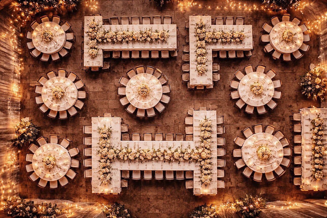 Vogelperspektive eines festlichen Hochzeitssaals. Runde und eckige Tische sind symmetrisch angeordnet und greifen wie Tetris-Steine perfekt ineinander. Warmes Licht und Blumenschmuck.