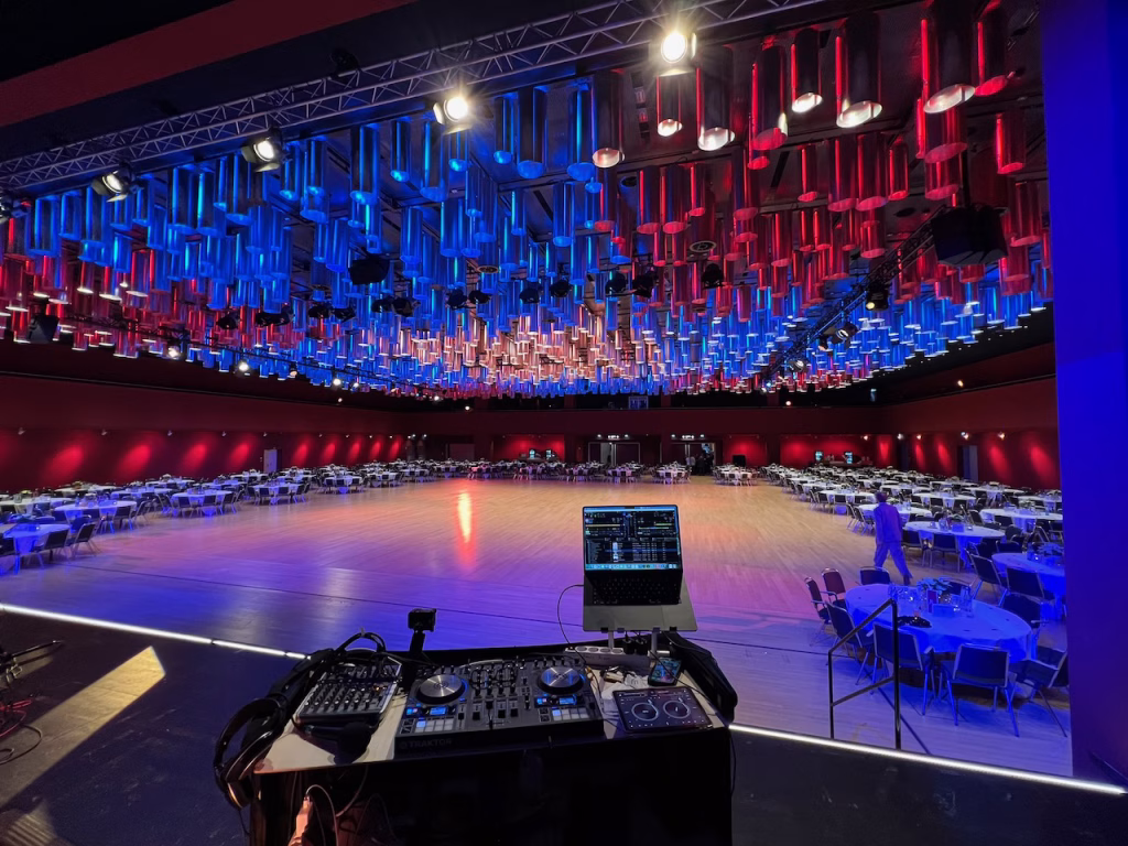 Blick vom DJ-Pult in den festlich beleuchteten, noch leeren Ballsaal des CCH Hamburg. Im Vordergrund das DJ-Equipment, an der Decke eine beeindruckende Lichtinstallation mit hunderten Röhren.