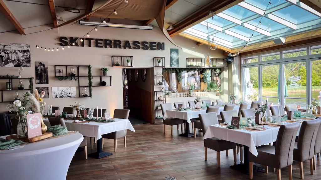 Heller Festsaal der Hochzeitslocation Skiterrassen Hooksiel mit gedeckten Tischen und Blick auf das Wasser.