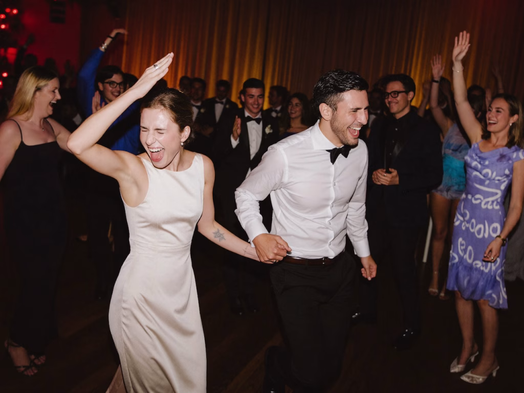 Ein glückliches Brautpaar kommt jubelnd auf die Tanzfläche und klatscht mit den feiernden Hochzeitsgästen ab.