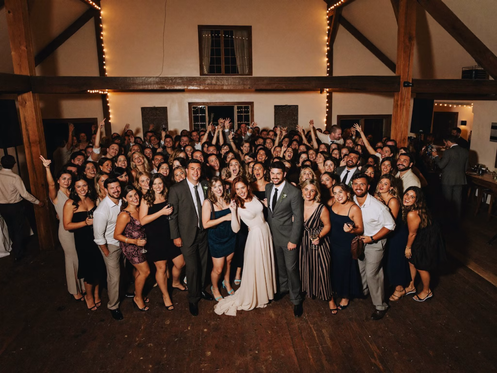 Eine lachende Hochzeitsgesellschaft drängt sich für ein gemeinsames Gruppenfoto dicht auf der Tanzfläche zusammen – eine clevere Eröffnungstanz Alternative.
