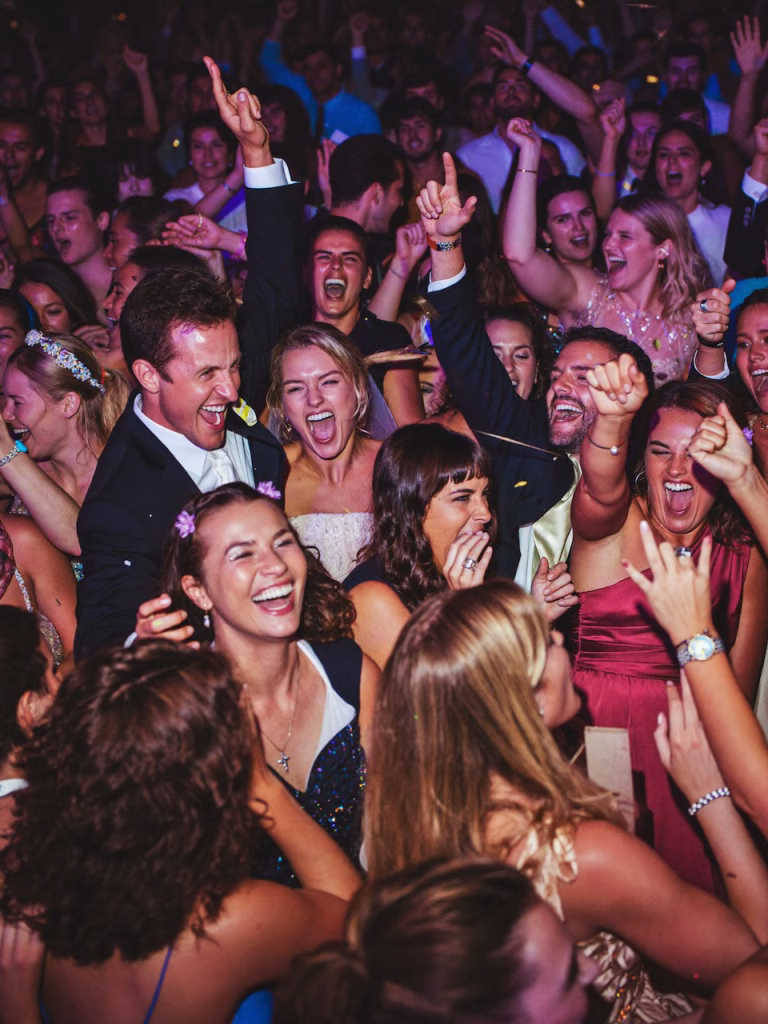 Eine Menschenmenge auf der Hochzeit rastet vor Freude auf der Tanzfläche aus, Hände in der Luft, Gesichter lachen und schreien.