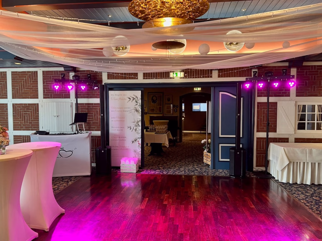Festsaal im Romantikhotel Bösehof mit DJ-Setup, lila Lichtanlage und Stoffdraping an der Decke bei einer Hochzeitsfeier