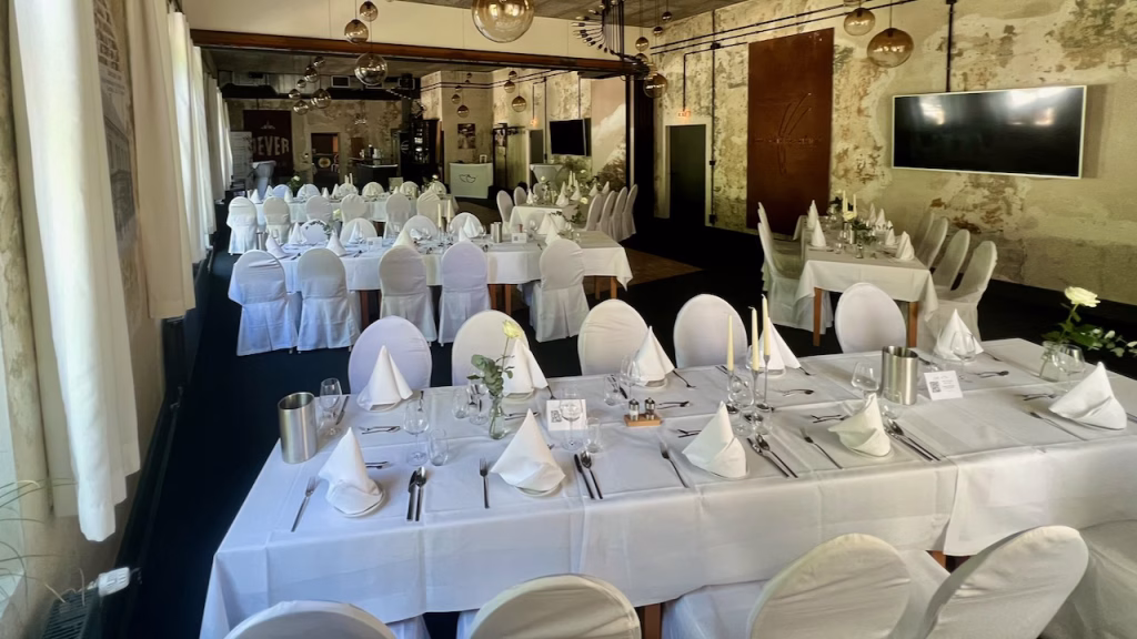 Festlich eingedeckter Saal im Schützenhof Jever mit Industrial-Charme, freigelegter Wand und Kronleuchtern bei einer Hochzeitsfeier