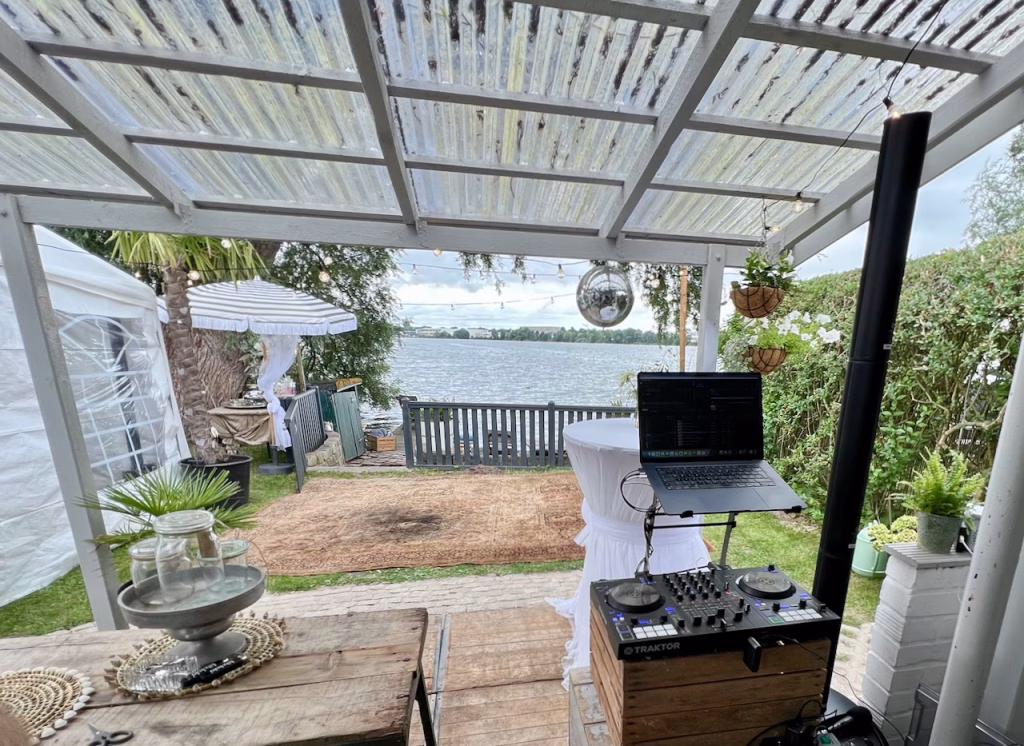 Kompaktes DJ-Setup mit Traktor-Controller unter einer Pergola am Banter See in Wilhelmshaven – im Hintergrund Tanzteppich und Seeblick